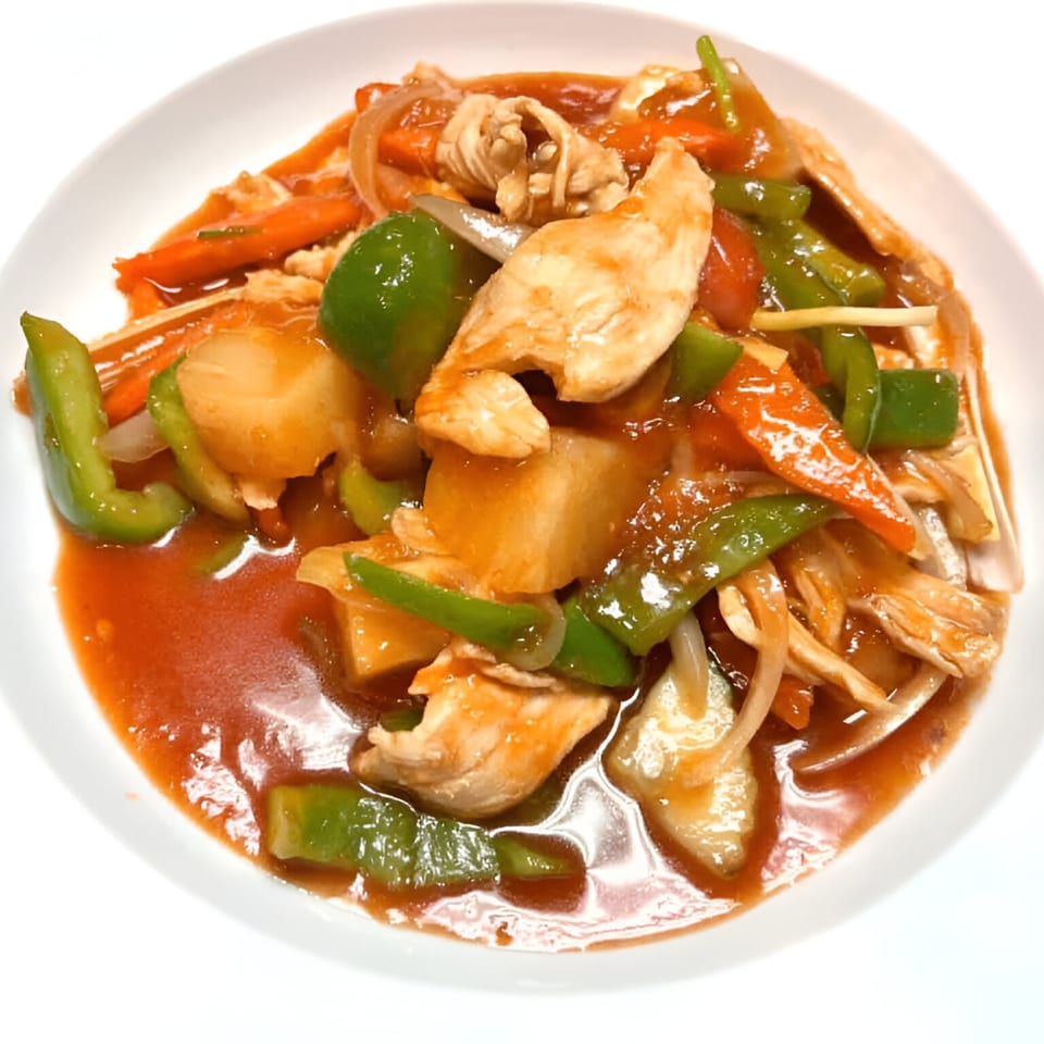 Sweet and sour chicken with bell peppers, carrots, and pineapple in a white bowl.