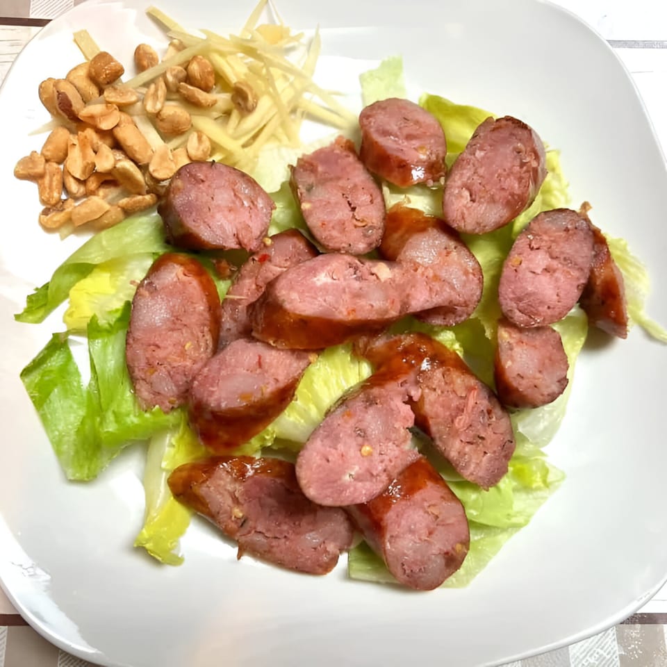 Sliced Thai sausage with lettuce, peanuts, and ginger on a white plate.