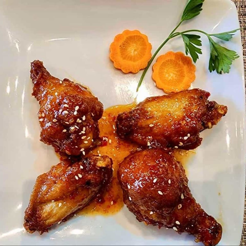 Four glazed Thai chicken wings with sesame seeds, garnished with carrot slices and parsley.